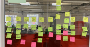 A number of post-it notes are organised on a glass wall with an office space in the background. The post-it notes reference elements of data culture.